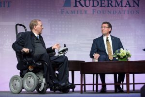 Congressman Jim Langevin sitting in his wheelchair, discussing Congressman Gregg Harper on the Summit stage. 